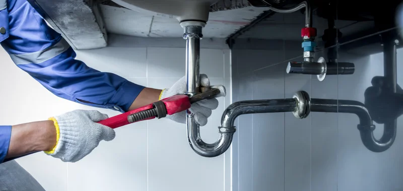 Professional plumber repairing kitchen sink pipes with a wrench Professional plumber repairing kitchen sink pipes with a wrench