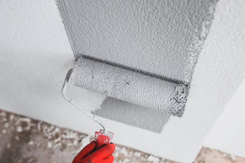 Paint roller applying gray textured paint to a white wall Paint roller applying gray textured paint to a white wall