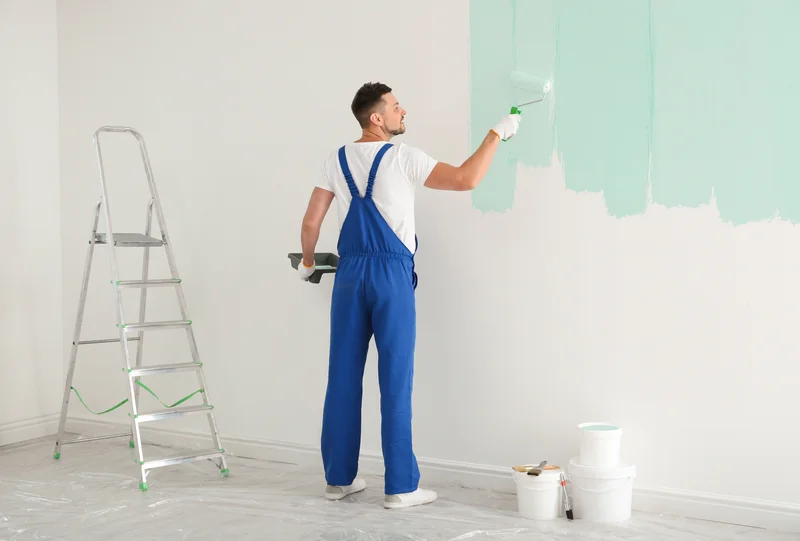 Interior painter using a roller to apply light green paint to wall Interior painter using a roller to apply light green paint to wall