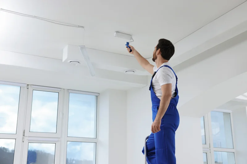 Professional painter on a ladder painting an interior room ceiling white.