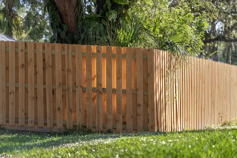 Newly installed wooden slat privacy fence in green yard Newly installed wooden slat privacy fence in green yard