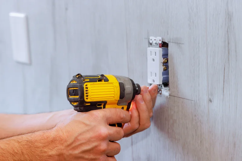 Hands using a yellow power drill to install a new electrical outlet on a wall. Hands using a yellow power drill to install a new electrical outlet on a wall.